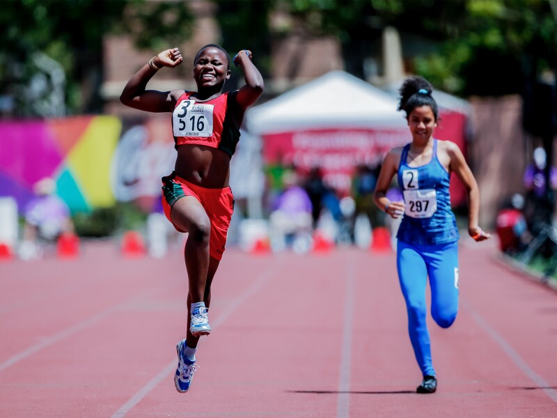 Auf dem Foto jubelt eine Läuferin bei der Leichtathletik. Im Hintergrund läuft noch eine weitere Sportlerin.