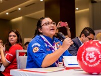 Das Foto zeigt eine Special Olympics Botschafterin mit einem Mikrofon. Sie spricht und alle hören ihr zu. Vor ihr liegt ein Fußball.