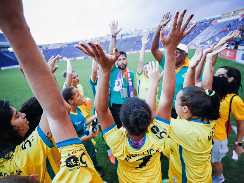 The photo shows athletes of a women's team raising their arms in the air and cheering.