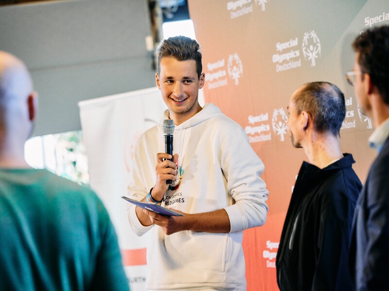 In the photo, Louis is seen with a microphone, talking to other people and laughing.