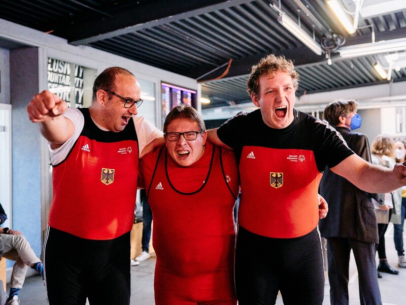 Auf dem Foto jubeln drei Special Olympcis Deutschland Athleten in die Kamera. Sie haben gerade erfahren, dass sie für das Team SOD bei den Weltspielen im Kraftdreikampf antreten dürfen.