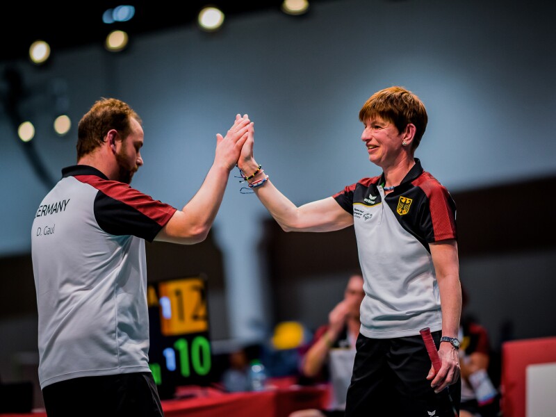 Das Foto zeigt zwei Badminton-Spieler*innen, die sich gerade ein High-Five auf dem Spielfeld geben.