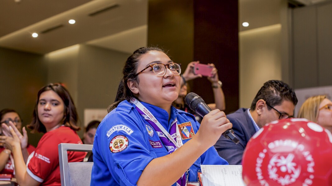 Auf dem Foto ist ein Frau zu sehen, sie spricht in ein Mikrophone und ist sehr freudig dabei