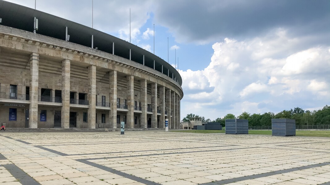 Das Foto zeigt das Olympiastadion in Berlin im Anschnitt und einen gepflasterten Vorplatz.