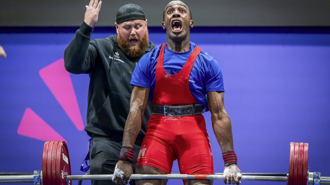 The photo shows an athlete doing powerlifting. His muscles are completely tense and he is moaning.