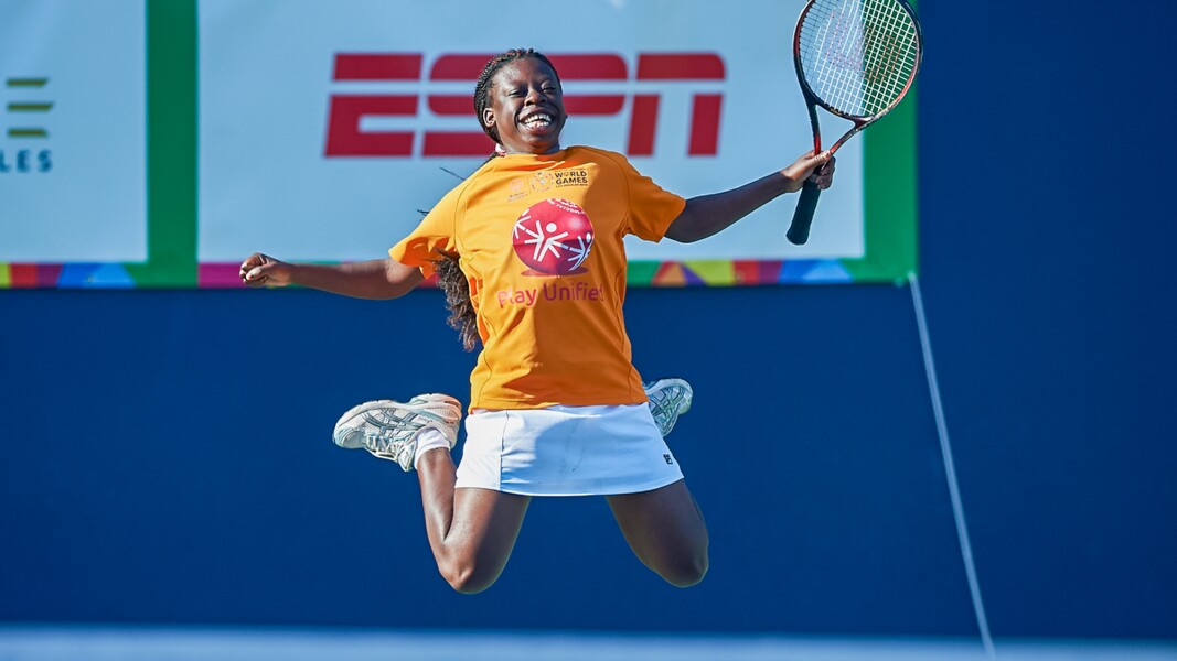 Das Foto zeigt eine Athletin beim Tennis. Sie hält einen Schläger in der Hand, freut sich und springt in die Luft.
