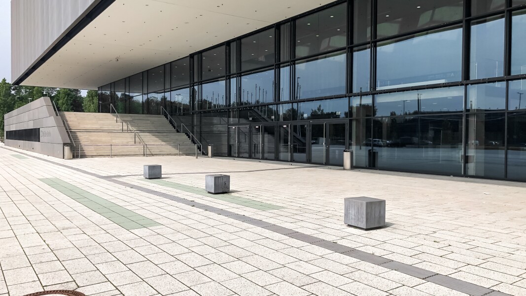 The photo shows a paved forecourt with a building with glass facade in the background and a wide staircase outside.