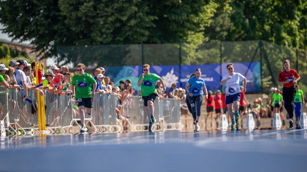 Auf dem Foto sieht man fünf Läufer*innen bei ihrem Wettbewerbe. Sie rennen und werden von zahlreichen Fans bejubelt.