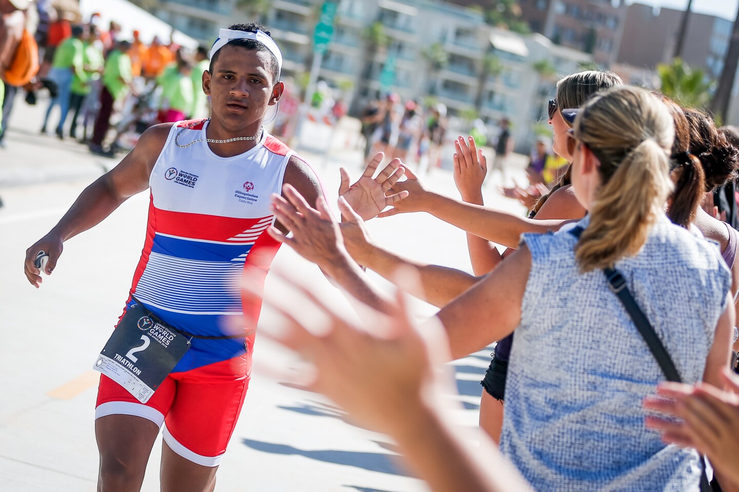 Das Foto zeigt einen Sportler beim Triathlon. Er rennt und klatscht mit den Zuschauer*innen ab.