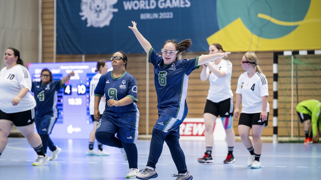 Das Foto zeigt mehrere Spielerinnen eines Handballspiels, die nach einem erfolgreichen Wurf jubelnd zurück Richtung Mittelkreis laufen. Dabei freuen sie sich und strecken ihre Arme nach oben in Siegerpose.