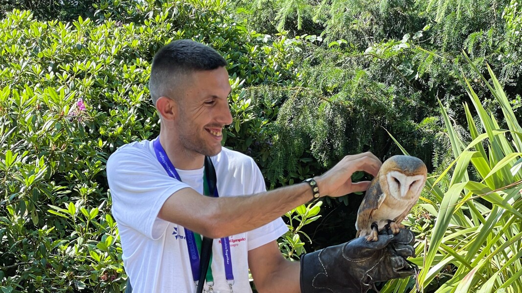 Das Foto zeigt einen Athleten aus Montenegro, der im Rahmen des Host Town Programs eine Eule auf der behandschuhten Hand trägt, die er lächelnd streichelt.