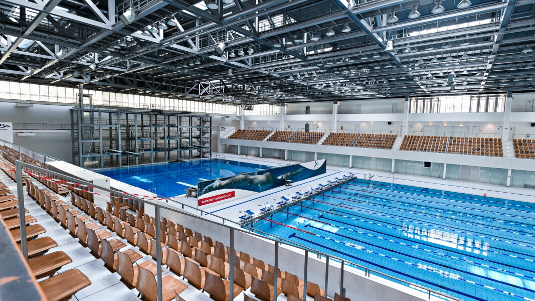 Das Foto zeigt die Schwimm- und Sprunghalle im Europasportpark. Es ist eine Aufnahme von oben. Man sieht die Sprungtürme und die Schwimmbahnen.