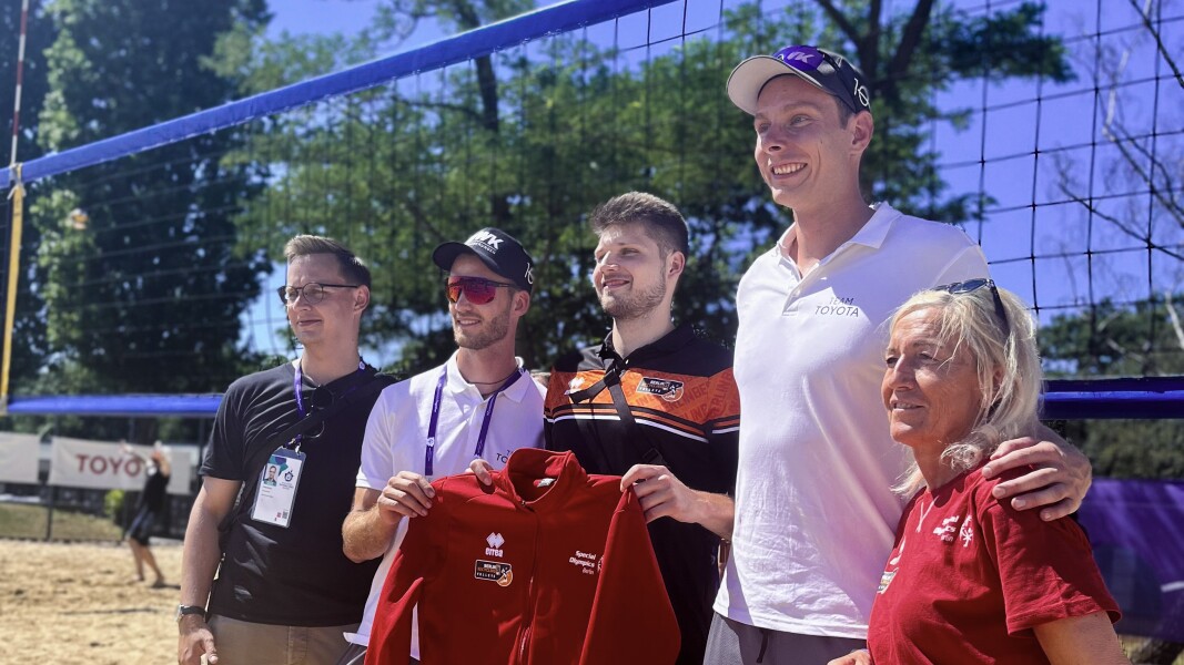 The photo shows beach volleyball pros Nils Ehlers and Clemens Winkler together with RB Volleys pro Ruben Schott at the National Games while attending the beach volleyball competitions. Two more people are standing next to them.