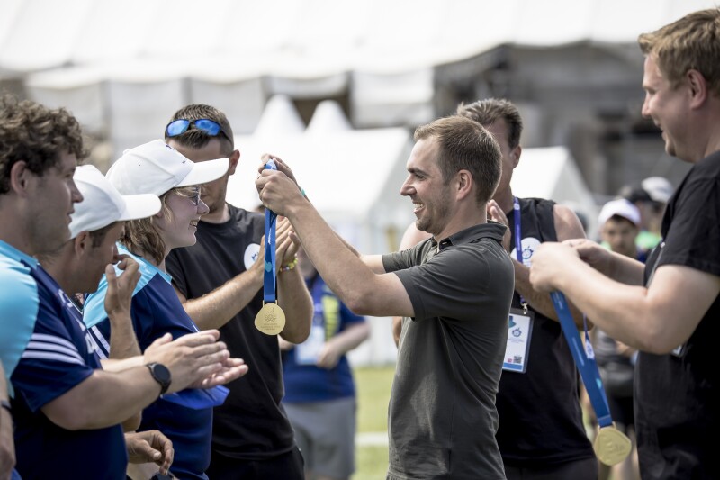 Das Foto zeigt den ehemaligen Fußballer Philipp Lahm während er bei den Nationalen Spielen Berlin 2022 Medaillen an Athlet*innen überreicht. Er hat dabei ein lächeln auf dem Gesicht.