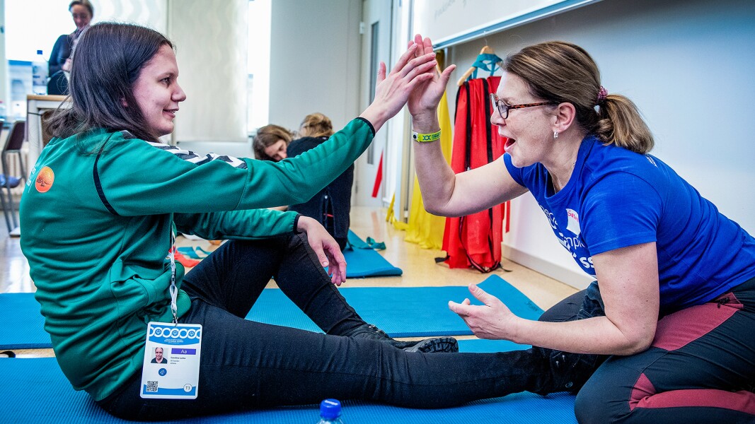 The photo shows two women giving each other a high five while sitting on a yoga mat.