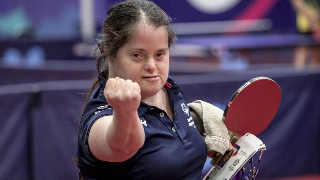 A girls hodling Table tennis racket , identity card and hand towel on her left hand where in her right hand is clenched and showing to the camera