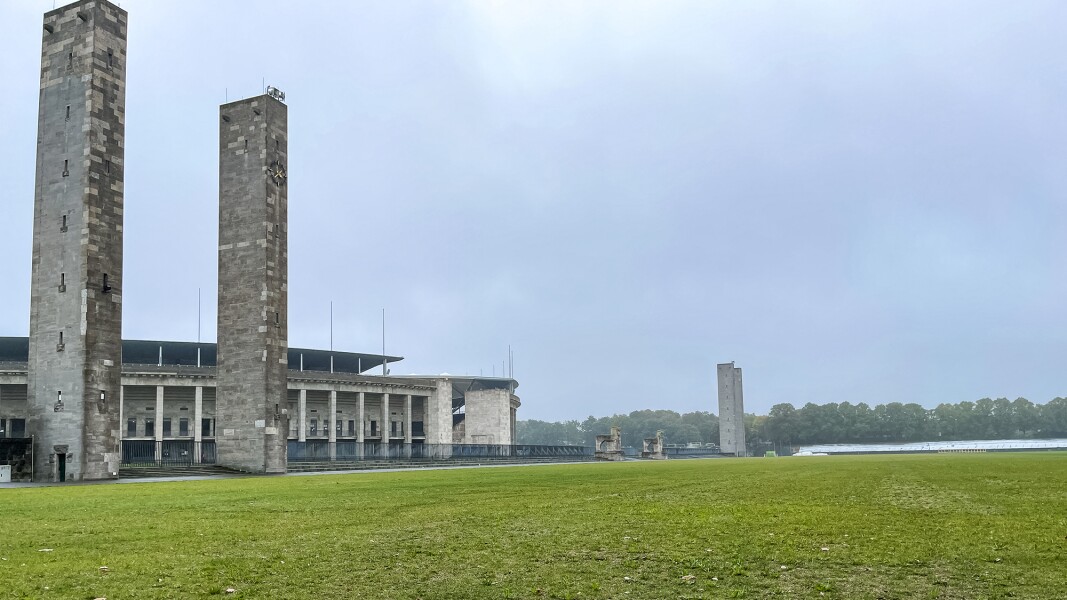 Das Foto zeigt eine Rasenfläche im Vordergrund und zwei große Säulen, sowie das Berliner Olympiastadion im Anschnitt.