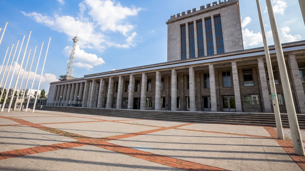 Das Foto zeigt einen gepflasterten Vorplatz und ein Gebäude mit Säulen auf dem Messe Berlin steht.