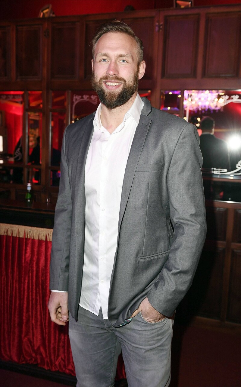 Das Foto zeigt den ehemaligen deutschen Diskuswerfer Robert Harting, der einen Anzug trägt und freundlich in Richtung Kamera lächelt.