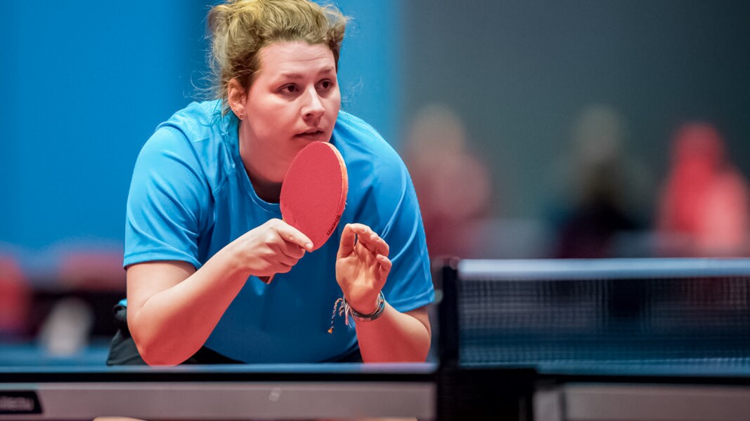 Das Foto zeigt eine Athletin beim Tischtennis. Sie ist konzentriert, hält ihren Schläger oben und erwartet den Ball.