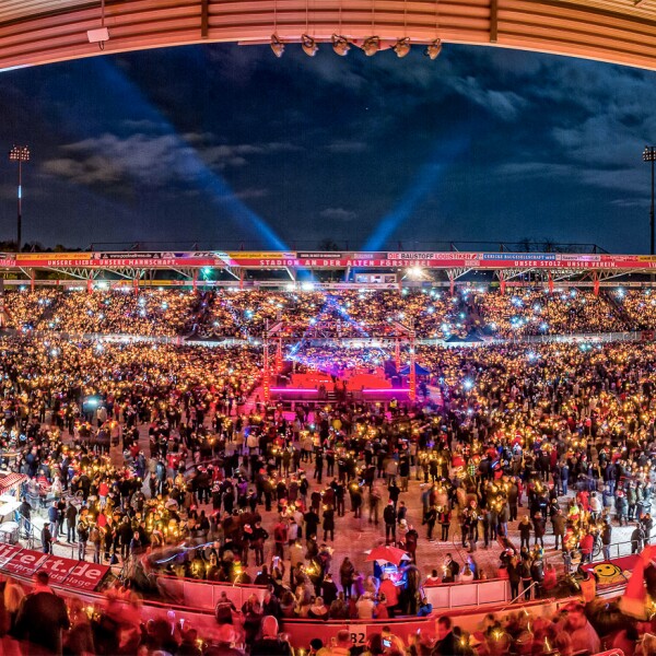 The photo shows the Stadion An der Alten Försterei filled with many people to a major event. The colors are bright in front of the evening sky.