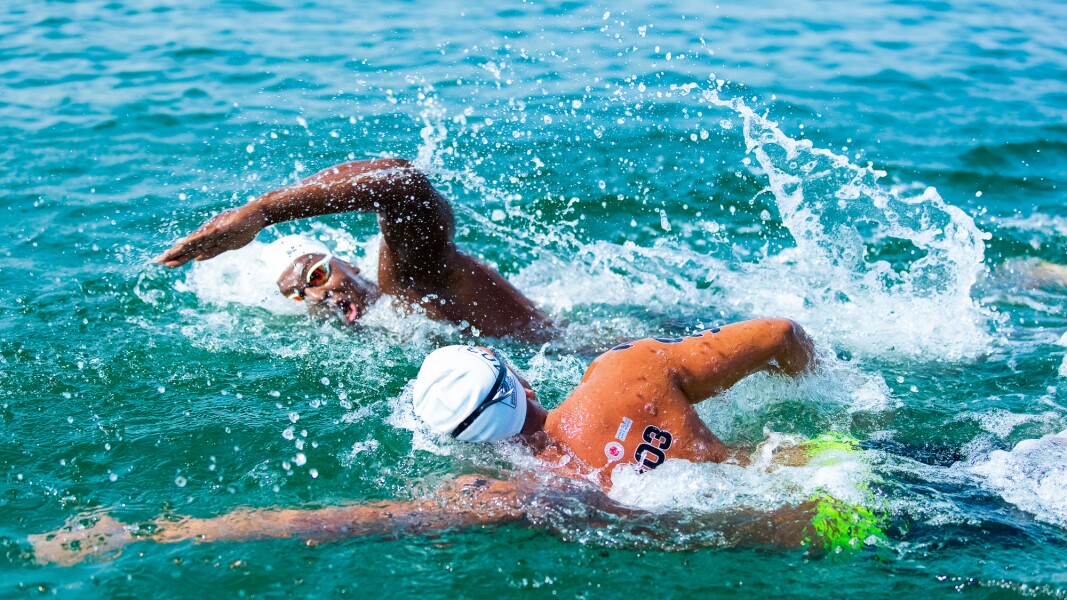 Das Foto zeigt zwei Athleten beim Freiwasserschwimmen. Das Wasser spritzt um sie herum.