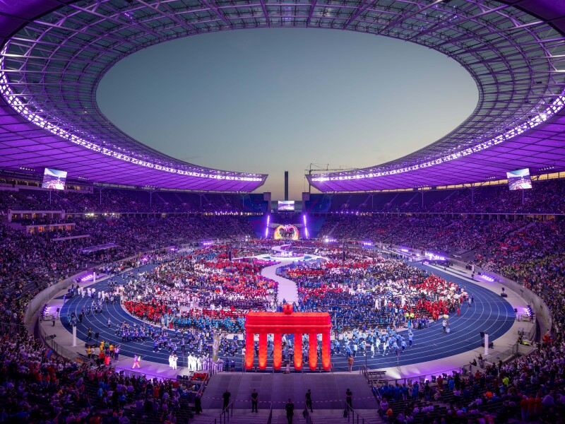 Das Foto zeigt das gesamte Olympiastadion bei der Eröffnungsfeier. Alle Delegationen sind in der Mitte und das Stadion leuchtet.