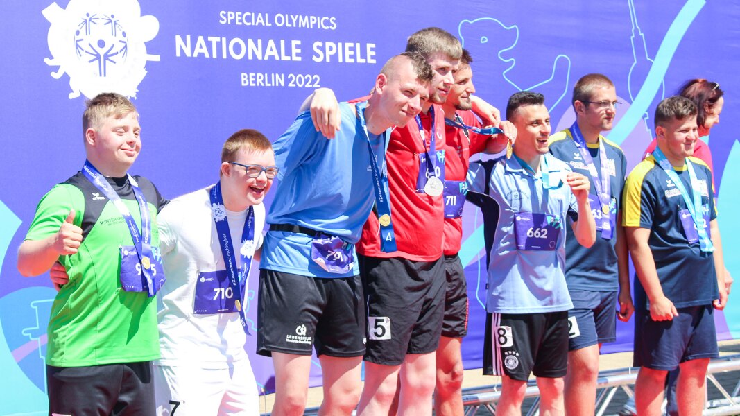 Das Foto zeigt 8 Athleten bei einer Siegerehrung. Sie liegen sich in den Armen und lächeln in die Kamera.