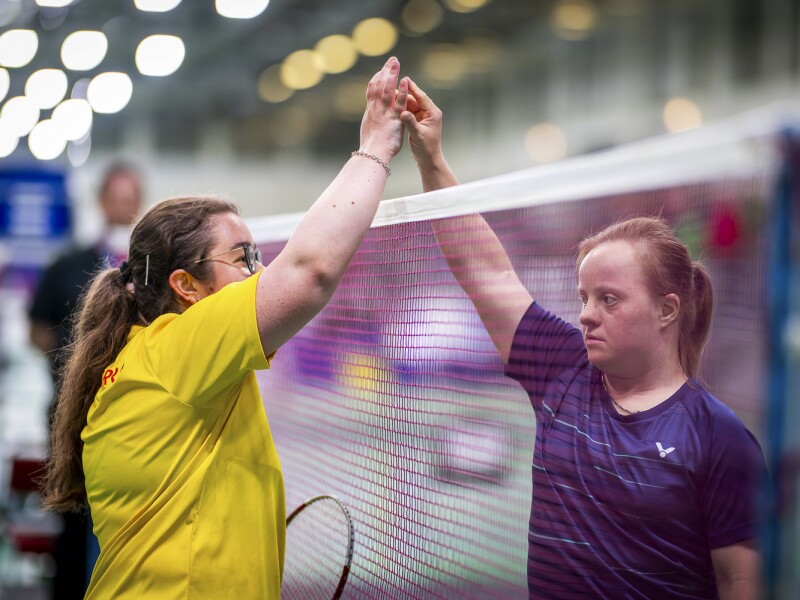 In the photo, two opposing players are high-fiving over the badminton net.