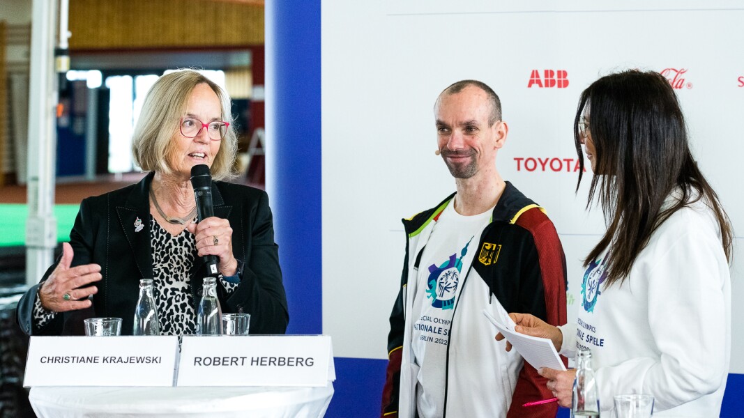 Das Foto zeigt einen Ausschnitt der Pressekonferenz. Darauf sind Christiane Krajewski, Präsidentin von Special Olympics Deutschland, sowie Robert Herberg, unser Gesicht der Spiele, zu sehen. Daneben steht außerdem Iris Spranger - die Senatorin für Inneres und Sport von Berlin.