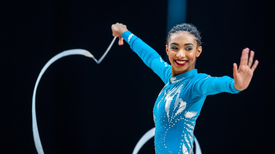 Das Foto zeigt eine Athletin bei der Rhythmischen Sportgymnastik mit einem Seil. Sie strahlt Freude aus und hat beide Arme angehoben.