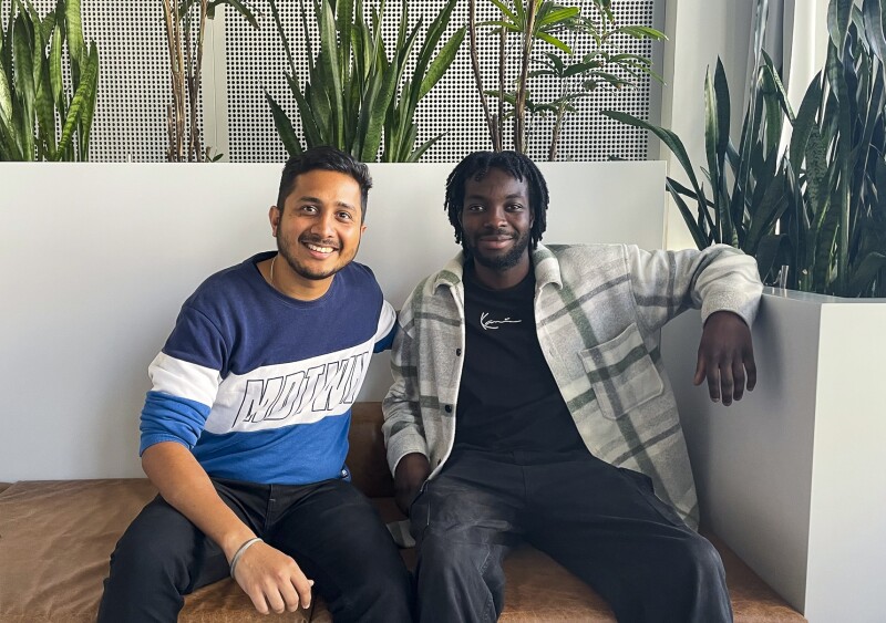 Das Foto zeigt Saurabh Mishra und Larry Boateng, beide Mitarbeiter im Weltspieleteam im Bereich Volunteers. Sie sitzen entspannt auf einem Sofa und gucken freundlich in die Kamera.