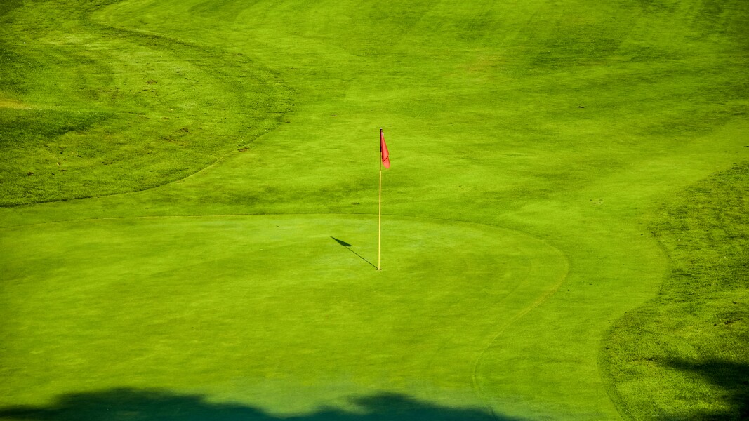 Das Foto zeigt einen Golfplatz mit leuchtend grünem rasen und einer roten Fahne beim Loch.