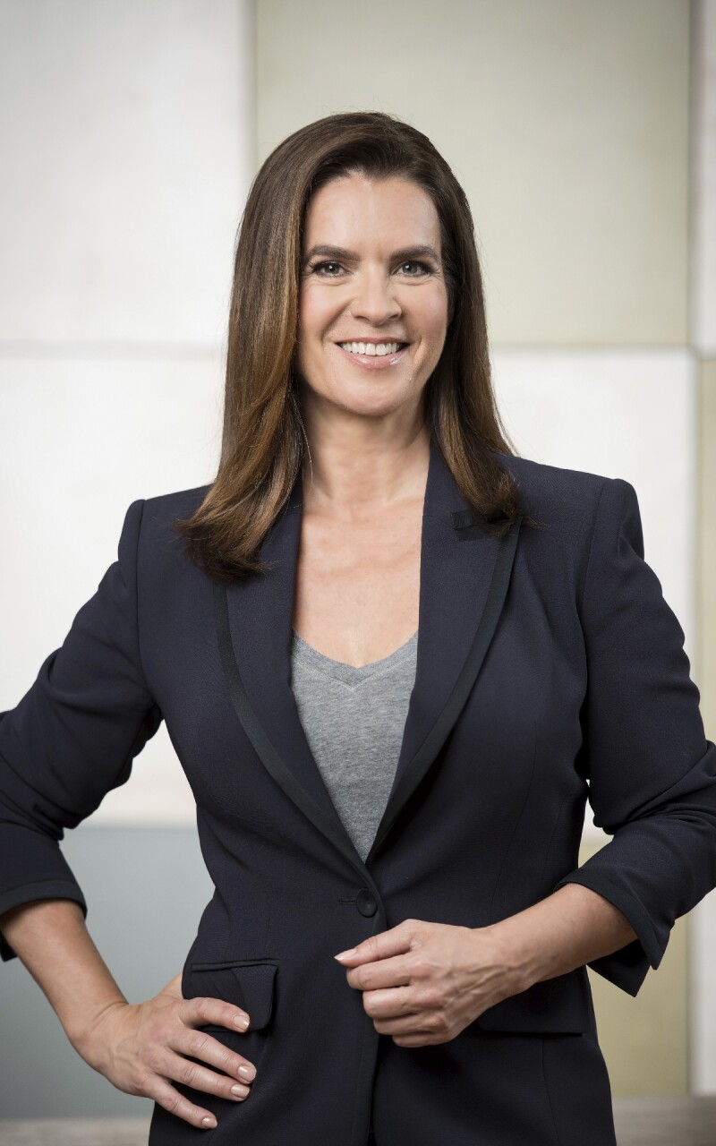 Das Foto zeigt die ehemalige deutsche Eiskunstläuferin Katarina Witt. Sie lächelt in die Kamera und trägt einen schwarzen Blazer.