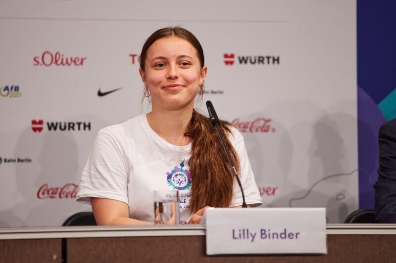 In the photo you can see one of our faces of the National Games: Lilly Binder. She is a Unified Partner at Special Olympics. Here she is smiling while actively participating in a press conference. 