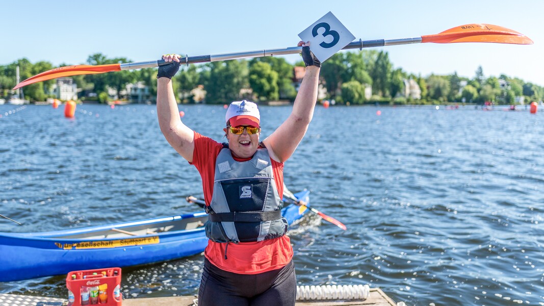 Das Foto zeigt die Kanutin Juliana Rößler nach ihrem Gewinn im Kanurennen während der Special Olympics Nationalen Spiele Berlin 2022. So hält jubelnd ihr Paddel über dem Kopf hoch.