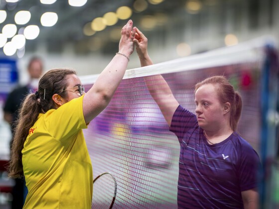 Auf dem Foto klatschen zwei gegnerische Spielerinnen über dem Badminton-Netz ab.