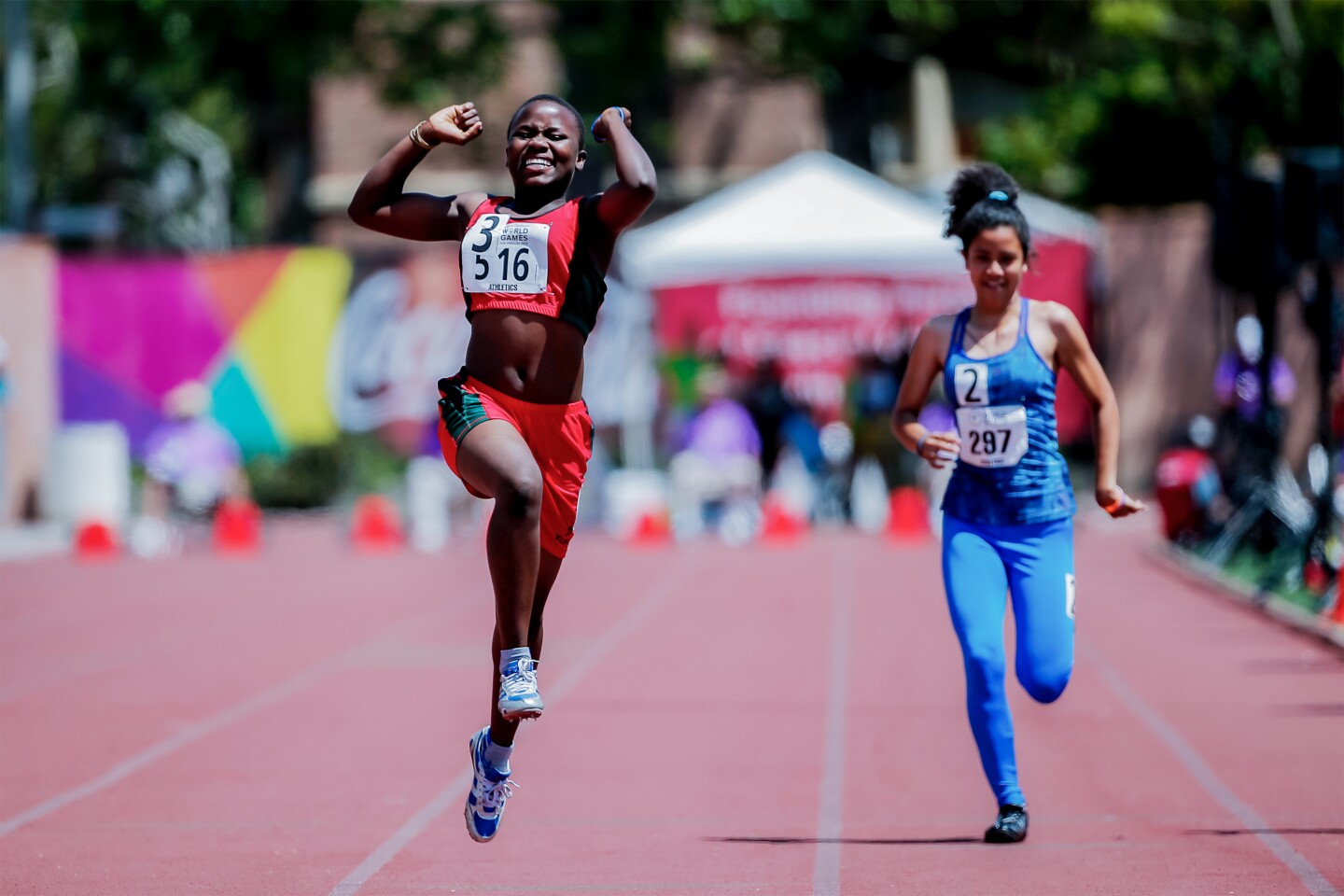 The photo shows two athletes on the track field, one jumping out of joy after finishing the competition first.