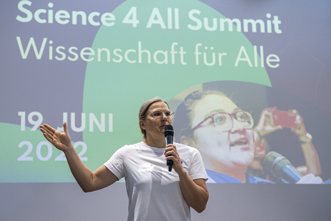 The photo shows a female speaker giving a lecture. She is speaking into a microphone