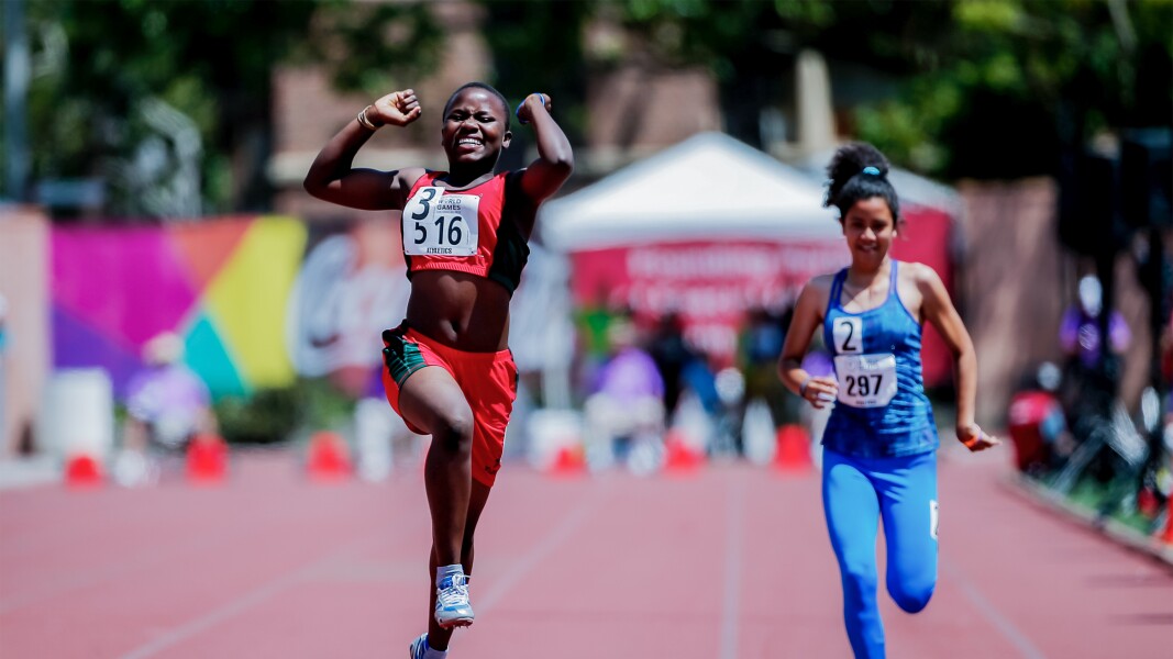 Auf dem Foto jubelt eine Läuferin bei der Leichtathletik. Im Hintergrund läuft noch eine weitere Sportlerin.