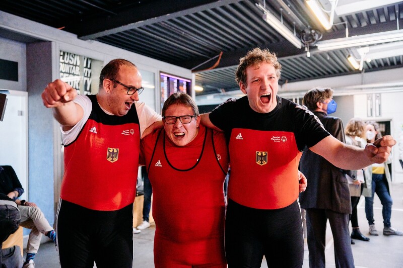 Auf dem Foto jubeln drei Special Olympcis Deutschland Athleten in die Kamera. Sie haben gerade erfahren, dass sie für das Team SOD bei den Weltspielen im Kraftdreikampf antreten dürfen.