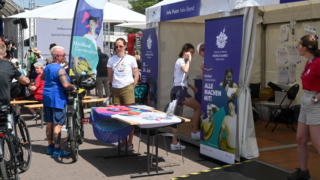 Auf dem Foto ist der Info Point zu den Weltspielen im Rahmen des Special Olympics Festivals der Nationalen Spiele zu sehen. Bunte Banner und Aufsteller machen auf das Riesenevent aufmerksam.