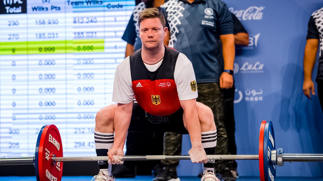 Das Foto zeigt einen Athleten beim Kraftdreikampf, der gerade kurz davor ist, ein Gewicht zu heben.