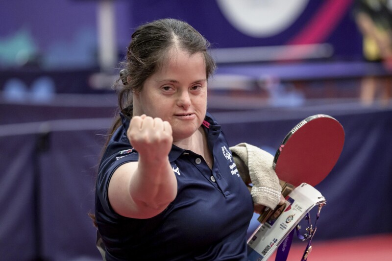 A girls hodling Table tennis racket , identity card and hand towel on her left hand where in her right hand is clenched and showing to the camera
