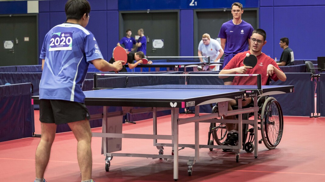 In the photo you can see two table tennis players playing. There is a coach in the background.