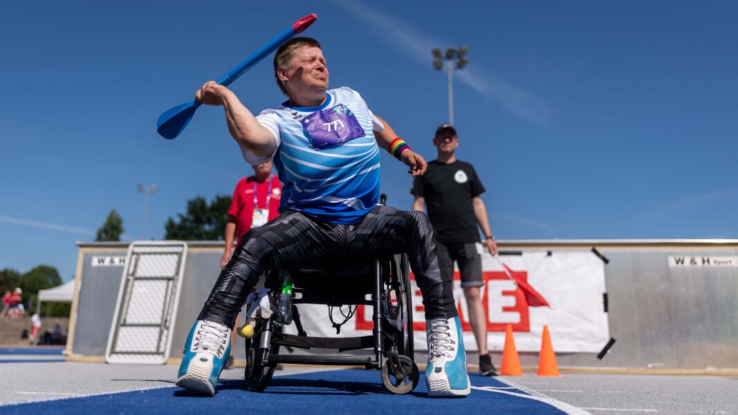 The photo shows an athlete performing Javelin throw at the National Games. She is sitting in a wheelchair and looks concentrated.