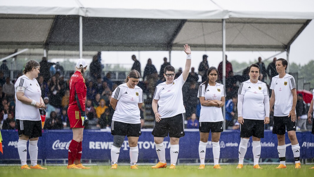 Auf dem Foto sieht man die deutsche Fußballnationalmannschaft der Frauen in offizieller Aufstellung vor dem Start des Spiels. Es regnet stark, aber alle scheinen trotzdem gut gelaunt.
