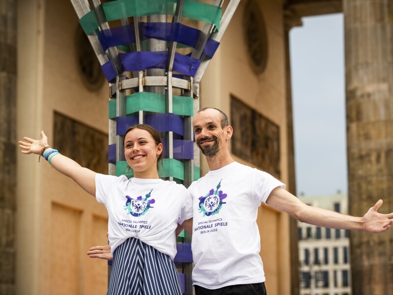 On the photo you can see our two faces of the games: Lilly Binder and Robert Herberg. They pose smiling and with outstretched arms in front of the big, freshly extinguished torch in front of the Brandenburg Gate during the Closing Ceremony.