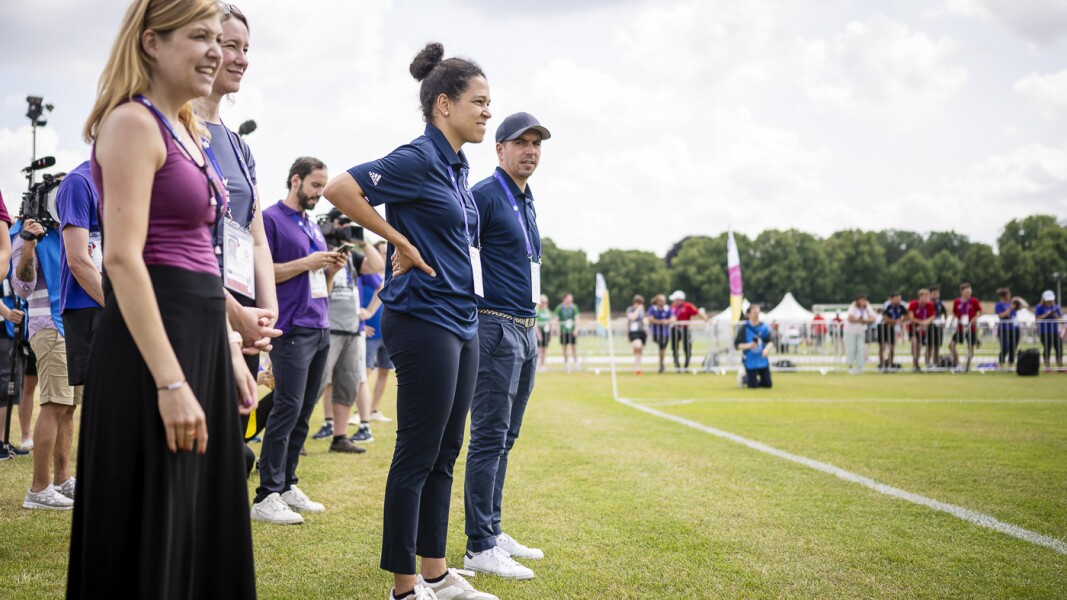 Das Foto zeigt die beiden Fußballer*innen Philipp Lahm and Celia Sasic beim Besuch des Fussballspiels Deutschland gegen Dänemark auf dem Maifeld. Beide stehen am Spielfeldrand und beobachten das Spiel sehr aufmerksam.