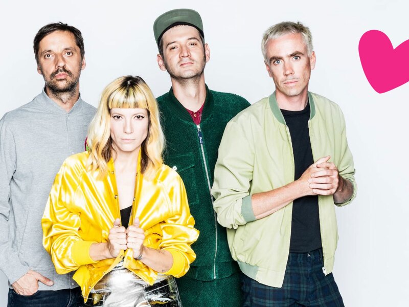 Das Foto zeigt die Berliner Band MiA., die bei der Eröffnungsfeier der Nationalen Spiele auftreten wird. Die vier Bandmitglieder schauen in die Kamera. In der Ecke ist zusätzlich ein rosa Herz platziert.